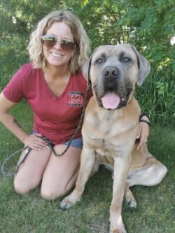 Debbi with a brown dog beside her. Debbi is wearing a red PrairieBurn K9 Academy company shirt